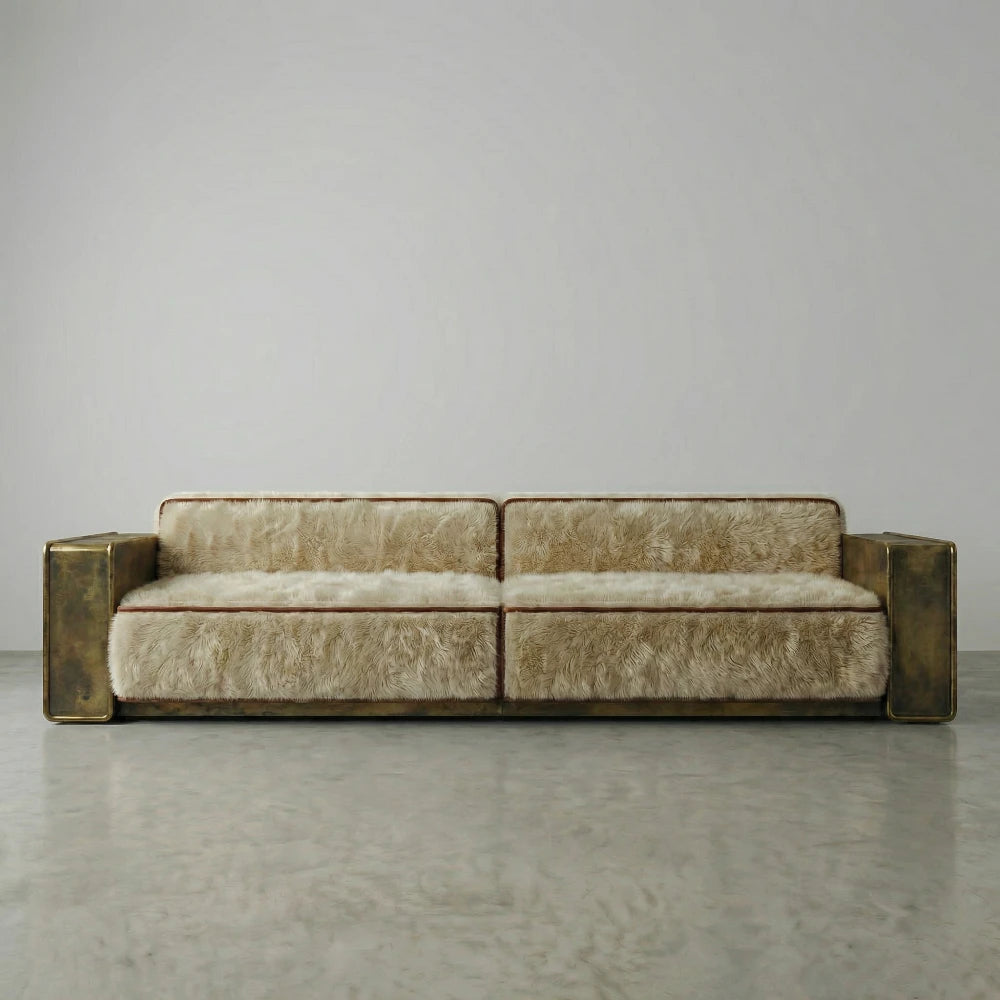 Front view of the Peau Sofa by Diamant Versatile, with cream furry upholstery, brown trim and broad gold-toned metal armrests.